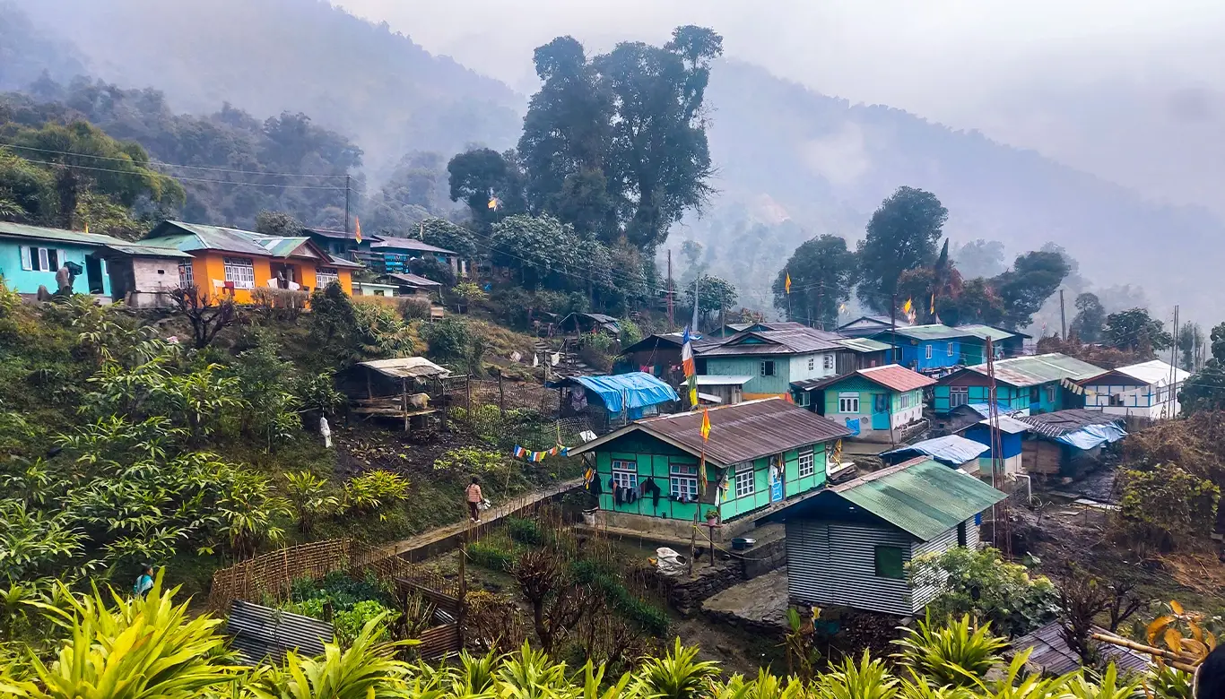 Scenic view of Labdang village in West Sikkim, showcasing colorful houses nestled on a hillside with lush greenery and mist-covered mountains in the background.